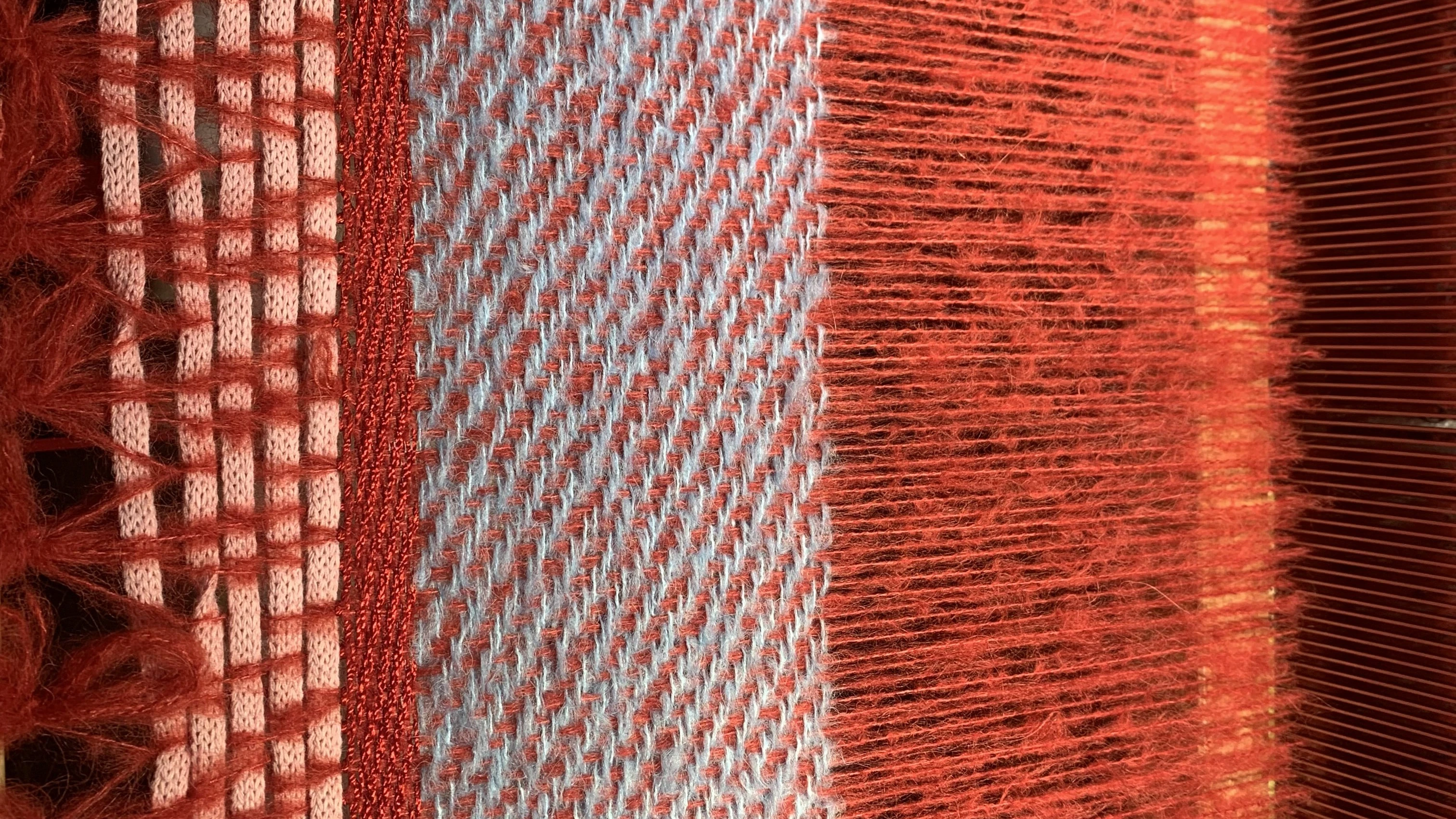 Tissage en cours sur le métier : trame bleu clair tissée rang après rang, chaîne mohair corail tendue jusqu'au peigne.