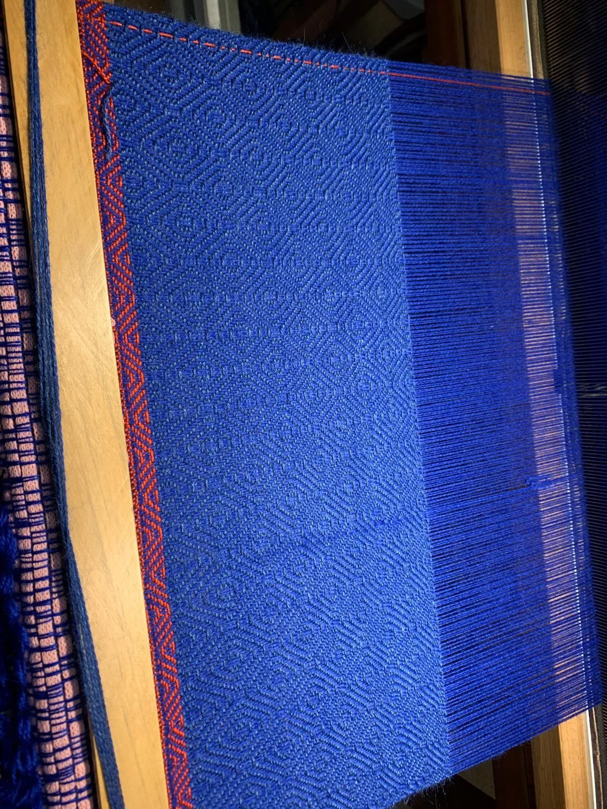 Tissage en cours sur le métier : motif de losanges bleu roi avec lisière rouge